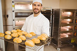 Baker smiling at camera holding rack of rolls