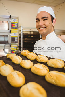 Baker smiling at camera holding tray of rolls