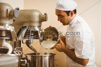 Baker pouring flour into large mixer