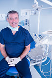 Smiling dentist in blue scrubs sitting in chair