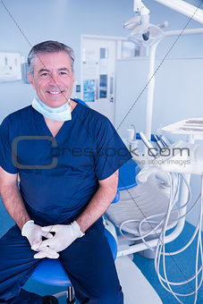Smiling dentist in blue scrubs sitting in chair