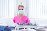 Dentist in mask wearing pink scrubs and looking at camera