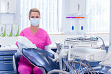 Dentist in pink scrubs looking at camera beside chair