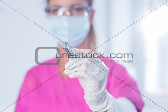 Dentist in surgical mask and scrubs holding tool