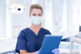 Dentist in mask using her tablet and looking at camera