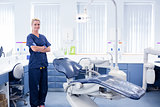 Dentist in blue scrubs standing with arms crossed beside chair