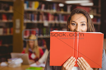 Pretty brunette student holding book in front of her face
