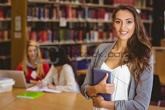 Pretty student holding tablet with classmates behind her