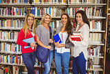 Smiling students standing beside shelf smiling at camera