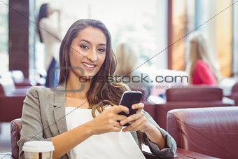 Smiling pretty brunette having coffee sending text