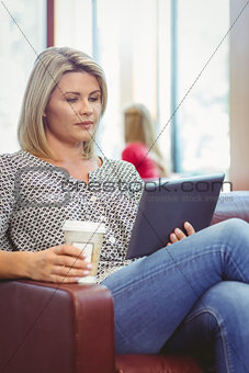 Woman using digital tablet and holding disposable cup