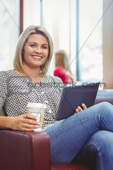 Smiling girl using digital tablet and holding disposable cup