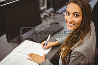 Smiling student sitting at desk writing on notepad