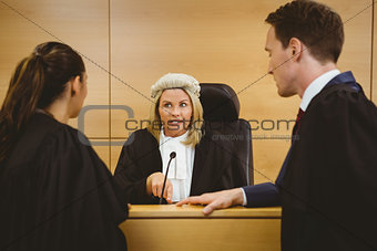 Judge wearing a dress and a wig speaking with lawyers