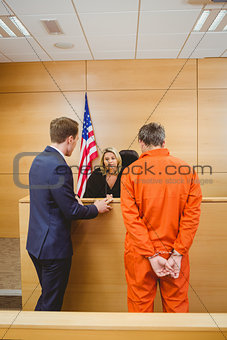 Lawyer and judge speaking next to the criminal in jumpsuit