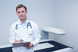Portrait of smiling doctor writing on clipboard