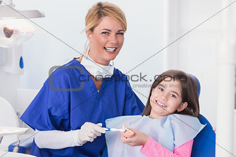 Smiling dentist teaching to her young patient how use toothbrush