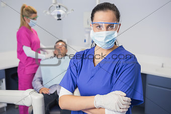 Dentist wearing surgical mask and safety glasses arms crossed