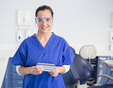 Smiling dentist with safety glasses holding teeth whitening