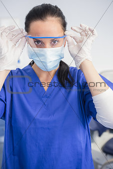 Dentist with surgical mask putting on her safety glasses