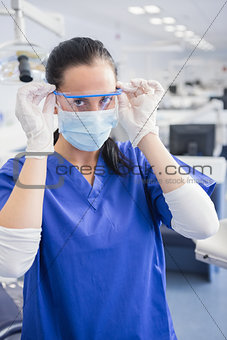 Dentist with surgical mask putting on her safety glasses