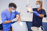 Dentist doing injection to his patient and nurse adjusting the light