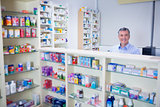 Pharmacist with grey hair standing behind shelves of drugs