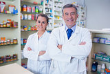 Smiling pharmacist and his trainee with arms crossed