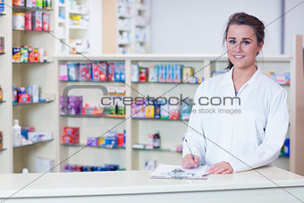 Smiling trainee in lab coat writing a prescription