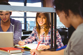 Happy student sitting at desk writing smiling at camera