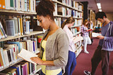 Students reading book against bookshelves