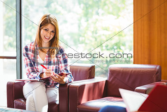 Happy student sitting on couch writing smiling at camera
