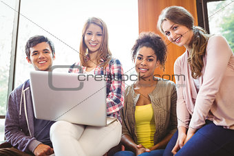 Smiling students sitting on couch using laptop
