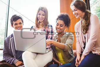 Smiling students sitting on couch using laptop