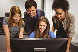 Smiling students sitting at desk using computer together