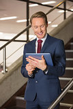 Handsome businessman standing on steps using tablet