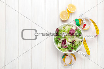 Fresh healthy salad, utensils and tape measure over white wooden
