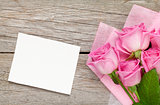 Pink roses bouquet and blank greeting card over wooden table