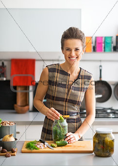 Portrait of happy young housewife pickling cucumbers in kitchen