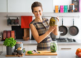 Portrait of happy young housewife showing jar of pickled cucumbe