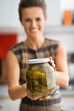 Closeup on happy young housewife showing jar of pickled cucumber