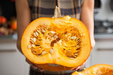 Closeup on young housewife in kitchen showing half of pumpkin