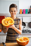 Portrait of happy young housewife showing half of pumpkin