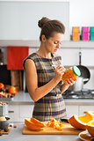Young housewife signing jar of pickled pumpkin in kitchen