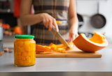 Closeup on jar of pickled pumpkin and young housewife cutting in