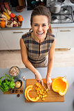 Portrait of happy young housewife cutting pumpkin in kitchen