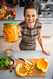 Portrait of happy young housewife showing jar of pickled pumpkin