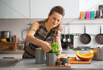Happy young housewife using fresh basil while cooking in kitchen