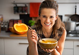 Happy young woman eating pumpkin soup in kitchen
