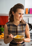 Happy young woman eating pumpkin soup in kitchen